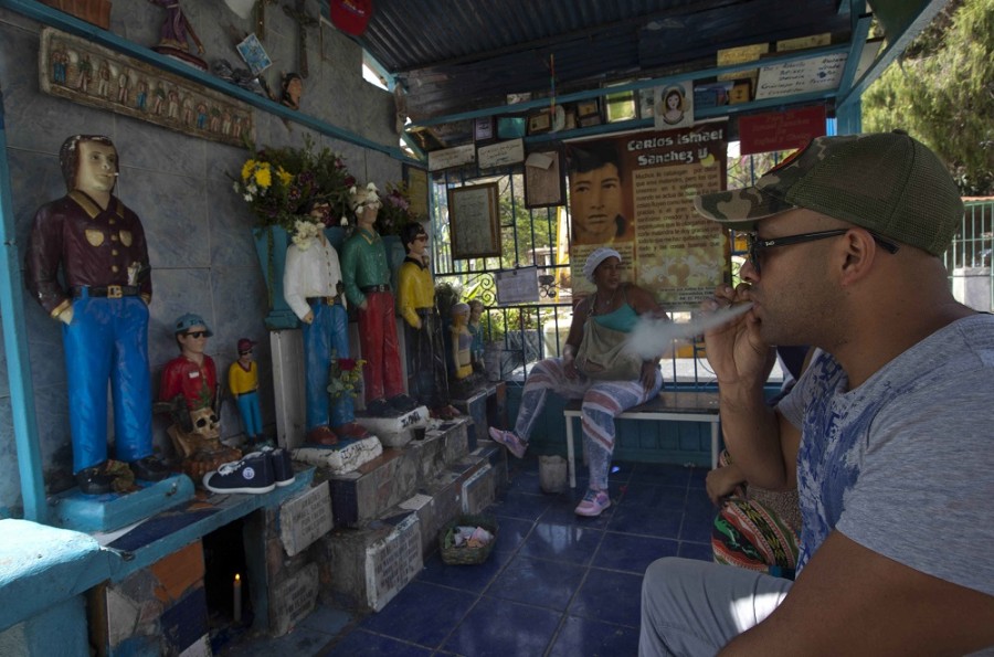 Un creyente fuma un cigarrillo ante las estatuas de Ismael en el mausoleo de los “Santos Malandros”  del Cementerio General ubicado en el barrio pobre de Guarataro en Caracas, Venezuela, el miércoles 1 de octubre de 2014. Los creyentes se reúnen en el cementerio, a veces por docenas, arrodillados en oración, bebiendo licor y fumando cigarrillos como ofrendas a la pequeña estatua del ladrón muerto. Foto AP/Ariana Cubillos.