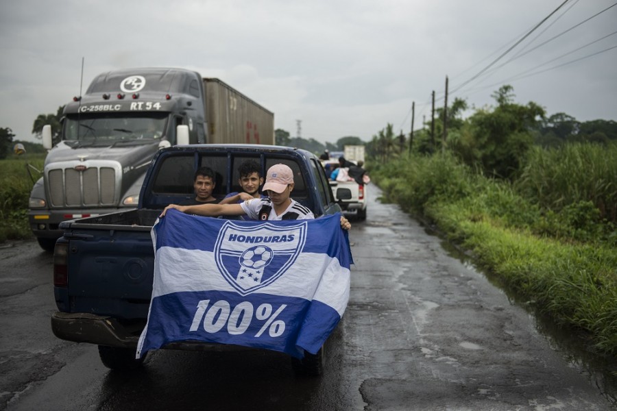 Un migrante sostiene una bandera nacional de Honduras, mientras va sentado en la parte trasera de una camioneta de carga de camino a la frontera con México, en Cocales, a unos 170 kilómetros al noroeste de la ciudad de Guatemala, Guatemala, el jueves 18 de octubre de 2018. Foto AP/Oliver de Ros.